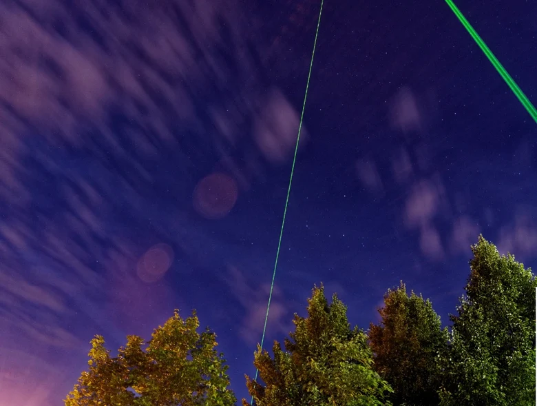 Drei grüne Laserstrahlen schießen in den violetten Himmel über Baumwipfel.