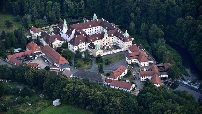 Ein barockes Gebäudeensemble mit hellen Fassaden, roten Ziegeldächern und einigen Türmchen mit hellgrüner Metalldeckung aus der Vogelperspektive